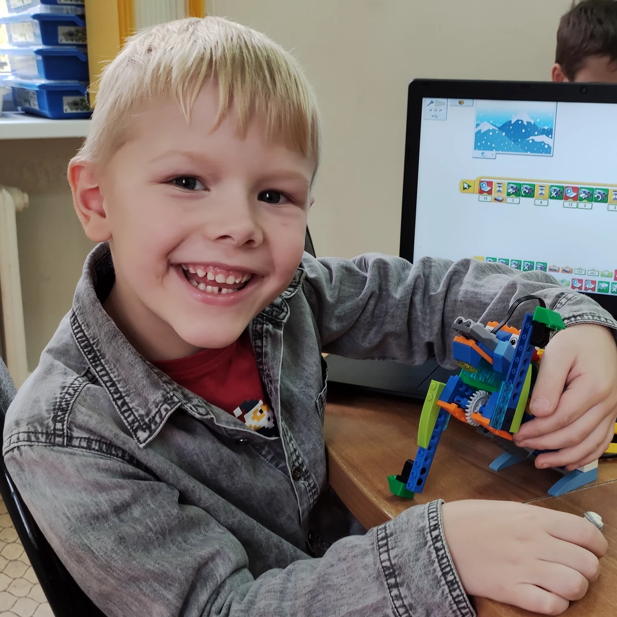 Улыбающийся ученик курса «Ниндзяго» показывает шагающую LEGO-модель у ноутбука