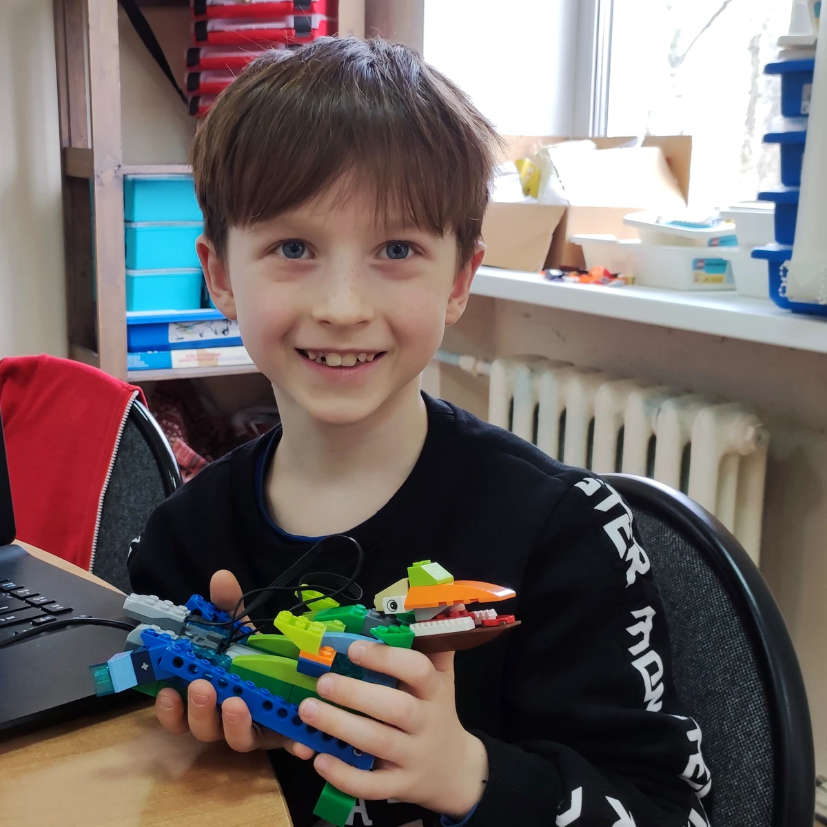 Ученик с LEGO-драконом рядом с программой на ноутбуке